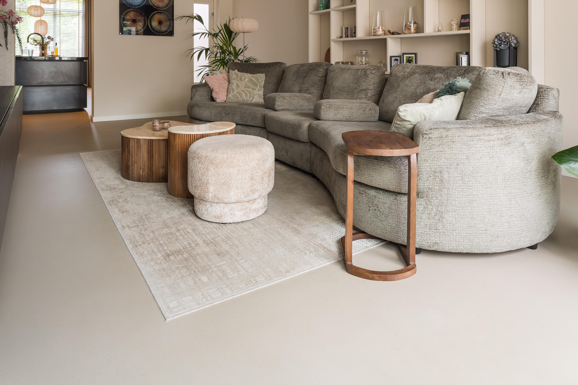 Overzicht woonkamer met micro terrazzo gietvloer grote bank en vloerkleed doorkijk naar keuken